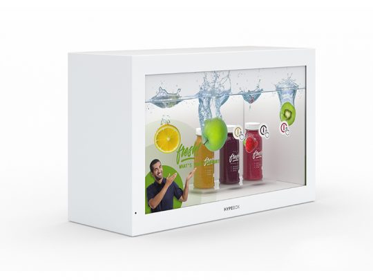 A white display box showcases three bottled fruit drinks with visible fruit slices and water splashes, while a man in a dark shirt gestures toward the beverages. The scene is presented on the 32 Zoll Full HD Hypebox Touch by Screensource (model HBT3210L), with vibrant, colorful graphics highlighting the interactive screen’s clarity.