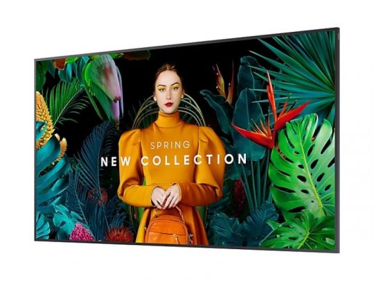 A woman in a vibrant orange outfit with a matching bag stands next to an 85 Zoll Smart Signage Display - Samsung QB85C for rent, surrounded by lush tropical plants. The digital display shows the text SPRING NEW COLLECTION. Perfect for advertising or showcasing seasonal fashion promotions with high-definition signage.