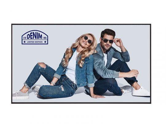 Two young adults wearing matching denim jackets and jeans, accessorized with sunglasses, sit casually on the floor against a plain background. A “Denim Limited Edition” logo appears in the top left corner. Both models look relaxed and stylish, highlighting trendy denim fashion.