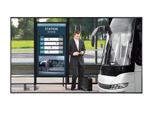 Business traveler at a modern bus stop with digital displays—A man in a suit checks his phone next to his suitcase while a white bus is parked nearby; electronic boards show real-time bus schedules and an event advertisement.
