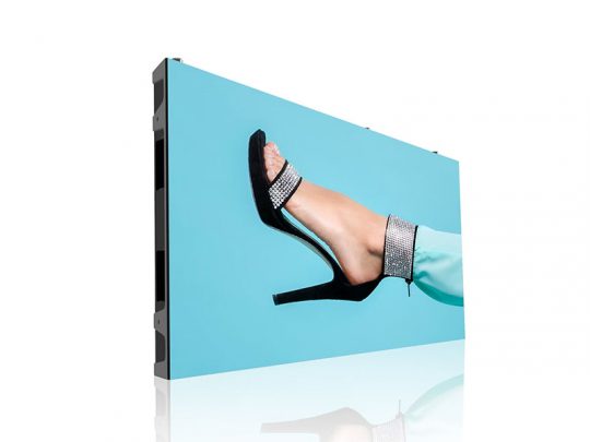 Digital display screen featuring a leg in aqua pants and a black high-heeled sandal with sparkling rhinestone accents, set against a blue background.
